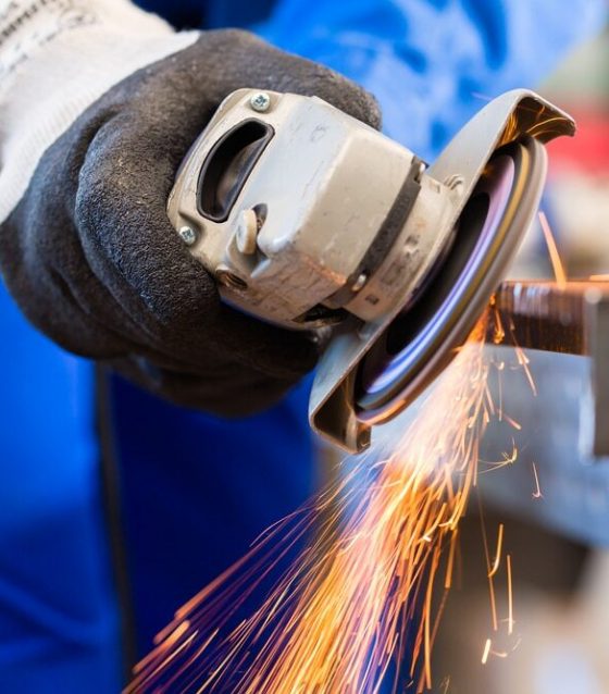 Hand Wearing Glove Using An Angle Grinder On A Piece Of Metal With Sparks Flying From Grinding